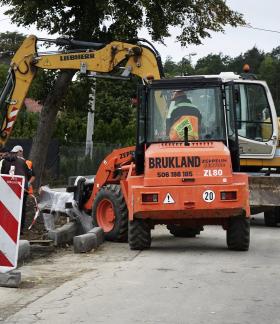 Pomarańczowa ładowarka kołowa z napisem Brukland oraz żółta koparka Liebherr na placu budowy drogi powiatowej Drzewica – Dąbrówka.