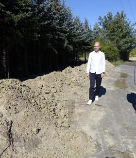  Burmistrz (po prawej) i Wiceburmistrz Drzewicy idą asfaltową drogą wzdłuż wykopu ziemnego i pasa iglastych drzew.