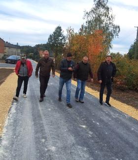 Pięciu mężczyzn idących nowo wybudowaną drogą asfaltową w Brzustowcu-Smugach w otoczeniu zabudowań i jesiennej zieleni. 