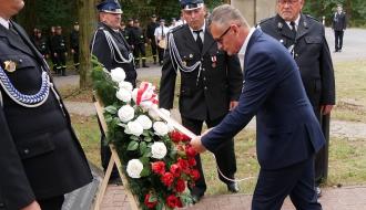 Przy asyście druhów OSP Burmistrz Drzewicy Janusz Reszelewski składa wieniec, poprawiając ułożenie biało-czerwonej szarfy. 