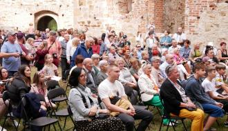 Liczna, kilkudziesięcioosobowa grupa widzów siedzi na krzesłach na zamkowym dziedzińcu.
