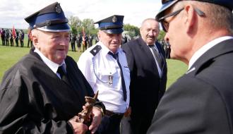 Na płycie boiska trzech druhów seniorów podczas ceremonii wręczenia statuetek św. Floriana. Z rąk Burmistrza Drzewicy statuetkę odbiera pierwszy druh od lewej. 