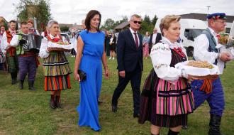 Korowód dożynkowy idący po trawie – na czele osoby w strojach ludowych z chlebami oraz przedstawiciele władz Gminy Drzewica. 
