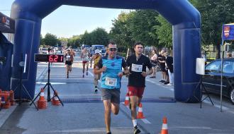 Dwaj mężczyźni w strojach sportowych wbiegają razem na metę biegu pod niebieską bramą.