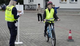 Filip Kmieciak (SP w Dzrewicy) przygotowuje się do wyjazdu rowerem na trasę Miasteczka Ruchu Drogowego. Po lewej nadzorująca starty policjantka