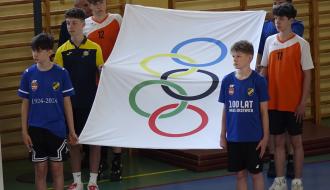 Sześciu uczniów w strojach sportowych trzyma flagę olimpijską