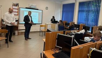 Przed siedzącymi w klasopracowni komputerowej młodzieżowymi radnymi stoją Zastępca Burmistrza Drzewicy Dominik Niemirski i Burmistrz Drzewicy Janusz Reszelewski, który zabiera głos na tle tablicy interaktywnej