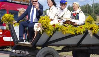 Na drewnianym wozie siedzą od lewej: machający ręką Burmistrz Drzewicy Janusz Reszelewski, Przewodnicząca Rady Miejskiej w Drzewicy Dorota Wiktorowicz, dożynkowy starosta Daniel Dąbrowski i dożynkowa starościna Marta Jakubczyk