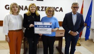 Na tle ściany z napisem GMINA DRZEWICA, godłem Polski i herbem Drzewicy od lewej stoją: Dyrektor ZEAS Małgorzata Kuchenbecker, trzymające plastikową promesę dwie nauczycielki SP w Drzewicy, Burmistrz Drzewicy Janusz Reszelewski.
