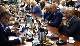 Uczestnicy sesji siedzą przy stołach w sali konferencyjnej Urzędu Miejskiego w Drzewicy. Głos zabiera Burmistrz Drzewicy Janusz Reszelewski (pierwszy po lewej, dolny plan).