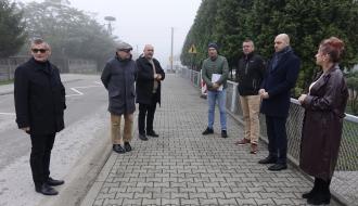 Uczestnicy odbioru – siedem osób – stoją na nowym chodniku między jezdnią a szkolnym ogrodzeniem