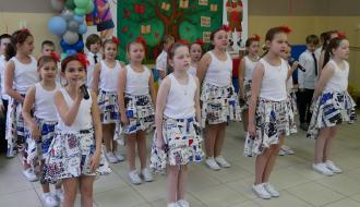 Występ artystyczny kilkunastoosobowej grupy uczniów SP w Drzewicy. Na przedzie dziewczęta w spódniczkach i białych koszulkach