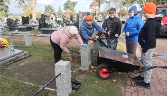 Prace porządkowe przy jednym z grobów na cmentarzu parafialnym w Drzewicy wykonuje pięć osób – dwie społeczniczki TPD i troje uczniów SP w Drzewicy. Pracujący korzystają z taczki, grabi i worków.