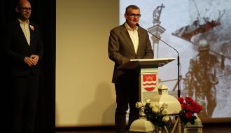 Na scenie przy mównicy stoi Burmistrz Drzewicy Janusz Reszelewski. Obok po lewej stoi Zastępca Burmistrza, Prezes DCW „Ofiarna dłoń” Dominik Niemirski