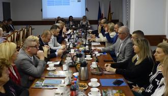 Uczestnicy sesji siedzą przy stołach w sali konferencyjnej Urzędu Miejskiego w Drzewicy. Z tyłu na środku stół prezydialny i ekran