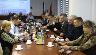 Uczestnicy sesji siedzą przy stołach w sali konferencyjnej Urzędu Miejskiego w Drzewicy. Z tyłu na środku stół prezydialny i ekran