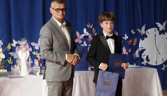 Burmistrz Drzewicy i uczeń w garniturze z dyplomem na tle dekoracji z motylami.
