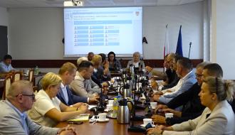  Sala obrad podczas sesji Rady Miejskiej w Drzewicy. Radni i przedstawiciele władz siedzą przy długim stole konferencyjnym. W tle widoczny ekran z porządkiem obrad