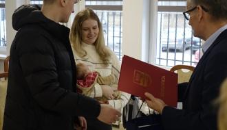 Burmistrz Drzewicy Janusz Reszelewski przekazuje gratulacje i prezent rodzicom trzymającym małe dziecko