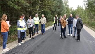 Na wyremontowanej drodze powiatowej stoją uczestnicy odbioru inwestycji – 12 osób. Przy drodze las