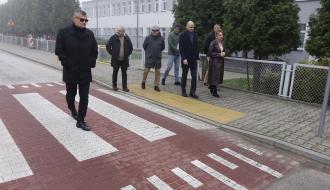Uczestnicy odbioru – siedem osób – idą chodnikiem oraz wyniesionym przejściem dla pieszych naprzeciwko szkoły w Domasznie