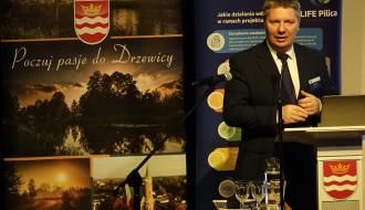 Wystąpienie stojącego na scenie przy mównicy Prezesa WFOŚiGW w Łodzi Piotra Kopka. Obok w tle ścianki promocyjne Gminy Drzewica i projektu LIFE Pilica.