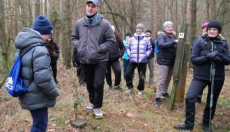 W lesie na szczycie Żurawiej Góry Maciej Bartos opowiada legendę o żurawiach. Wokół stoją słuchający go piechurzy.