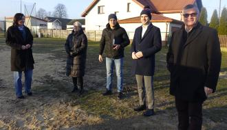 Pięć osób biorących udział w odbiorze inwestycji stoi na piaszczysto-trawiastym podłożu na tle domu