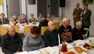 Uczestnicy spotkania siedzą za stołami. Po prawej stronie stoją: przemawiający Burmistrz Drzewicy oraz Zastępca Burmistrza.