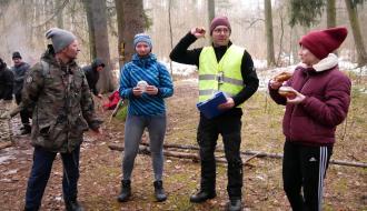 Na leśnej polanie do startu w konkursie jedzenia pączków na czas przygotowują się dwie piechurki i jeden piechur. Uczestników instruuje Wiceprezes LGD Andrzej Krzyżanowski