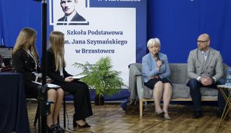 Panel dyskusyjny podczas Forum. Siedząc do mikrofonu przemawia Pani Wojewoda Łódzki, obok niej siedzi Dyrektor Biura Wojewody. Po lewej stronie dwie uczennice z notatkami przygotowują się do zadawania pytań. W tle baner z napisem „Szkoła Podstawowa im. Jana Szymańskiego w Brzustowcu” oraz hasłem „Z przeszłości w przyszłość”. Na podłodze stoi roślina doniczkowa, a całość odbywa się w sali o charakterze szkolnym.