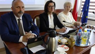 Prezydium Rady Miejskiej w Drzewicy. Przy stole prezydialnym siedzą od lewej: Wiceprzewodniczący Paweł Małek, Przewodnicząca Dorota Wiktorowicz, Wiceprzewodnicząca Joanna Popis. Przed nimi znajdują się mikrofony, tablety z herbem Drzewicy, napoje oraz filiżanki.