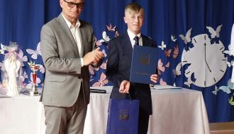 Burmistrz Drzewicy klaszcze obok nastoletniego ucznia trzymającego dyplom i torbę z herbem Drzewicy