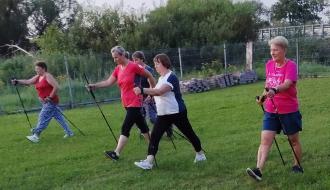 Grupa kobiet maszeruje z kijkami do nordic walking po trawiastym terenie
