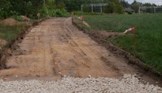 Wykorytowany odcinek drogi gruntowej wyznaczony palikami z taśmą ostrzegawczą, przygotowany pod podbudowę.