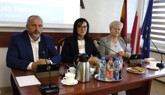 Prezydium Rady Miejskiej w Drzewicy. Przy stole prezydialnym siedzą od lewej: Wiceprzewodniczący Paweł Małek, Przewodnicząca Dorota Wiktorowicz, Wiceprzewodnicząca Joanna Popis. Przed nimi znajdują się mikrofony, tablety z herbem Drzewicy, napoje oraz filiżanki.