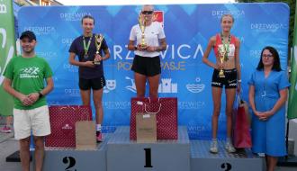 Na podium z pucharami i nagrodami trzy najlepsze biegaczki w kategorii open kobiet. Po lewej przy podium stoi Zastępca Burmistrza Drzewicy Dominik Niemirski, po prawej Dyrektor Banki Spółdzielczego w Przysusze – Oddziału w Drzewicy Ewa Jakubczyk