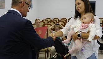 Burmistrz Drzewica Janusz Reszelewski wręcza list gratulacyjny trzymającej dziecko mamie