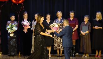 Kierownik WTZ Drzewica Sylwia Gąsiorowska odbiera kwiaty od uczestnika zajęć WTZ. Z tyłu kadra Warsztatu – 8 pań.