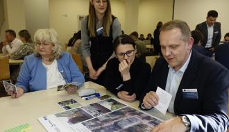 Część warsztatowa w sali audio-wideo RCK. Przy stole siedzą dwie kobiety i jeden mężczyzna. Między dwiema paniami stoi koordynatorka warsztatów