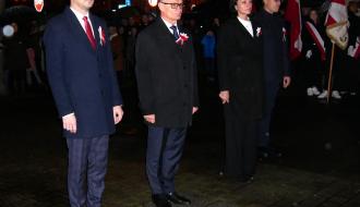 Przed Pomnikiem Pamięci w parku na Placu Wolności stoi delegacja samorządu Gminy Drzewica – od lewej: Zastępca Burmistrza Drzewicy Dominik Niemirski, Burmistrz Drzewicy Janusz Reszelewski, Przewodnicząca Rady Miejskiej w Drzewicy Dorota Wiktorowicz i Jacek Pecyna z Urzędu Miejskiego w Drzewicy. W tle biało-czerwone flagi i uczestnicy obchodów