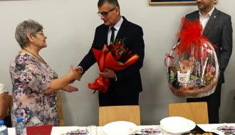 Burmistrz Drzewicy Janusz Reszelewski wręcza bukiet kwiatów Przewodniczącej Koła Emerytów i Rencistów Jadwidze Gapys. Po prawej stronie stoi Zastępca Burmistrza Dominik Niemirski, który trzyma kosz słodkości.