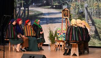Na scenie siedem pań z KGW Idzikowice w opoczyńskich pasiakach odgrywa scenkę pt. „Nabożeństwo maryjne – tradycyjna ludowa majówka przy figurce”