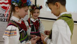 Opłatkiem łamią się dwie dziewczynki i chłopiec z zespołu „Mali Drzewiczanie”. Wszyscy ubrani w stroje opoczyńskie.