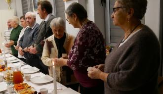 Przy stołach stoi osiem osób, trzymając w dłoniach opłatki