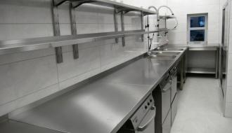 W pomieszczeniu kuchennym nowoczesny sprzęt, urządzenia i półki w kolorze srebrnym