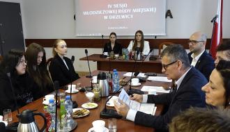 W sali konferencyjnej Urzędu Miejskiego w Drzewicy przy stole po lewej stronie siedzą trzy radne MRM w Drzewicy, natomiast po prawej stronie władze samorządowe Gminy Drzewica, w tym Burmistrz Drzewicy Janusz Reszelewski, który przemawia do mikrofonu.  Z tyłu siedzi Prezydium MRM w Drzewicy na tle ekranu