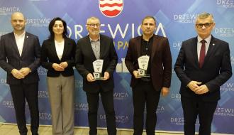 Na tle ścianki promocyjnej Gminy Drzewica stoją od lewej:  Zastępca Burmistrza Drzewicy Dominik Niemirski, Przewodnicząca Rady Miejskiej w Drzewicy Dorota Wiktorowicz, sołtys Trzebiny Stefan Pabijanek ze statuetką „Gospodarza Dożynek Gminnych 2026”, sołtys Świerczyny Karol Siedlecki ze statuetką „Gospodarza Dożynek Gminnych 2026” oraz Burmistrz Drzewicy Janusz Reszelewski.