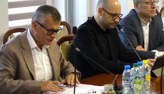 Trzech uczestników sesji siedzi przy stole konferencyjnym. Burmistrz Drzewicy odczytuje dokument, pozostali  - Zastępca Burmistrza i jeden z radnych - słuchają i korzystają z tabletów.