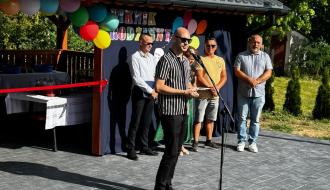 Zastępca Burmistrza Drzewicy przemawiający do mikrofonu przed drewnianą altaną. Za nim stoją pozostali uczestnicy oficjalnej części wydarzenia.